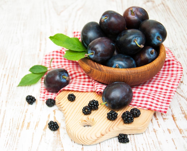 Ciruelas púrpuras frescas y moras en el fondo de madera