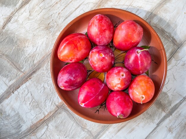 Ciruelas rojas miel maduras en un plato de cerámica marrón