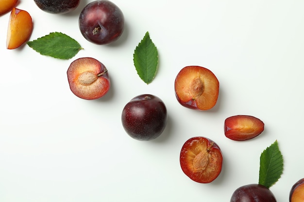 Ciruelas sabrosas con hojas sobre fondo blanco.