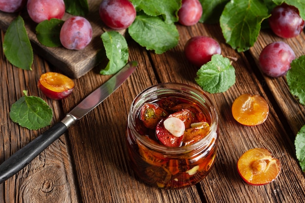 Ciruelas secas en un frasco de vidrio con aceite de oliva con ajo y especias. Conservas caseras, deshidratación. Primer plano, vista superior sobre fondo de madera vintage