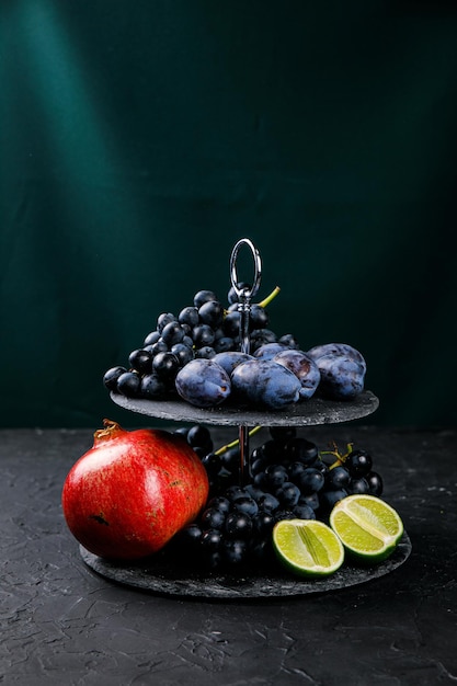 Ciruelas y uvas en un pedestal sobre un fondo oscuro