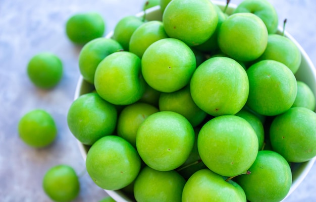 Ciruelas verdes en un recipiente sobre fondo de mármol. Foto de vista superior de frutas de ciruela.