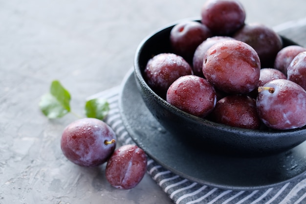 Ciruelas violetas frescas en el fondo de la mesa gris oscuro