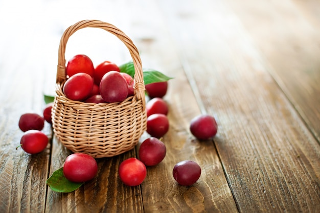 Ciruelos rojos maduros en una cesta de mimbre en una tabla de madera.