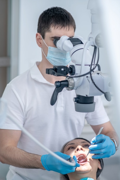 Cirugía dental. Cirujano dental masculino que trabaja con el paciente y que utiliza un instrumento médico óptico