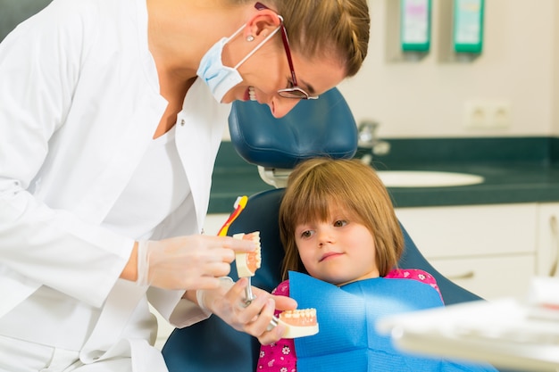 La cirugía de dentista sostiene la dentadura y explica a un niño paciente con un cepillo de dientes