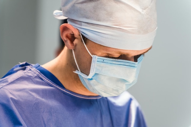 Cirugía de medicina y concepto de personas médico o cirujano masculino con máscara protectora sobre fondo borroso de cerca