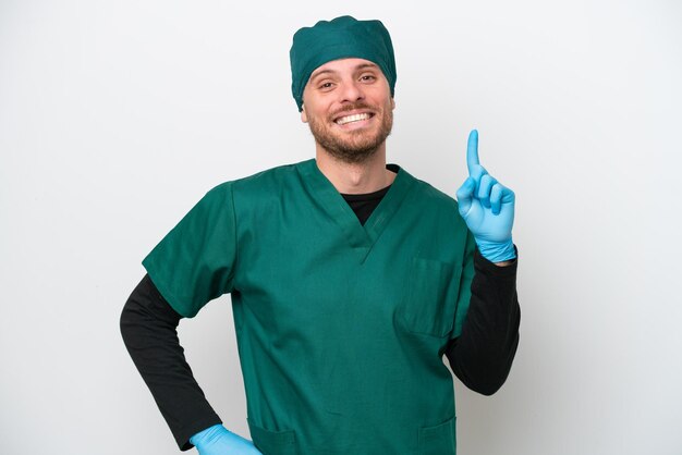 Cirujano brasileño con uniforme verde aislado de fondo blanco mostrando y levantando un dedo en señal de lo mejor