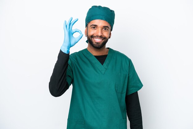 Cirujano brasileño con uniforme verde aislado de fondo blanco que muestra el signo de ok con los dedos