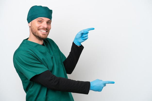 Cirujano brasileño con uniforme verde aislado de fondo blanco señalando con el dedo al costado y presentando un producto