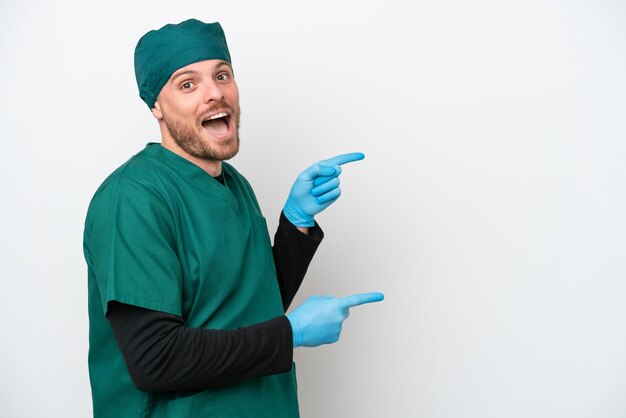 Cirujano brasileño con uniforme verde aislado de fondo blanco sorprendido y apuntando hacia el lado