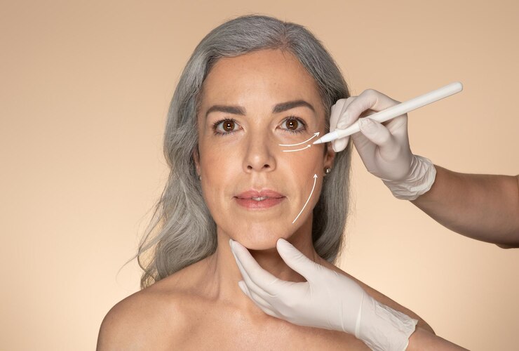 Foto cirujano dibujando líneas de perforación con lápiz en la hermosa cara de mujer mayor semidesnuda para plástico