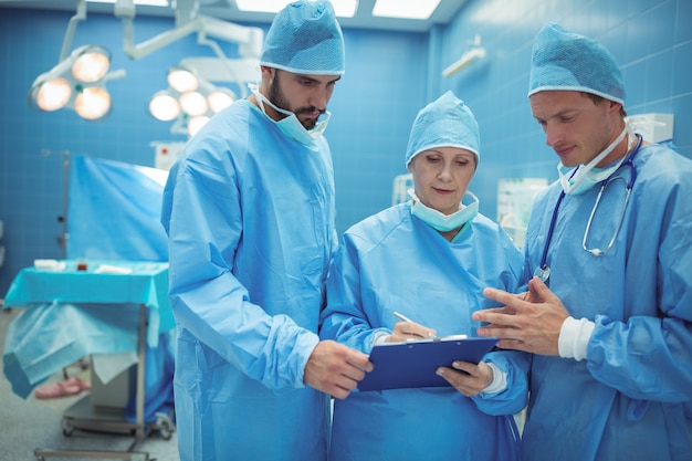 Cirujano masculino y femenino discutiendo sobre portapapeles en quirófano