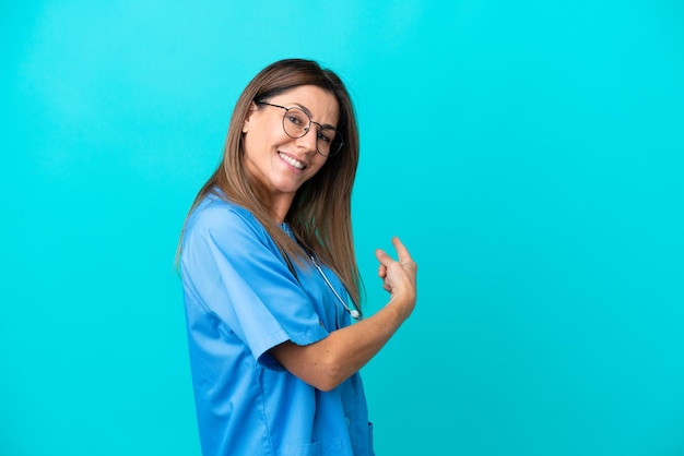 Cirujano de mediana edad mujer aislada sobre fondo azul apuntando hacia atrás