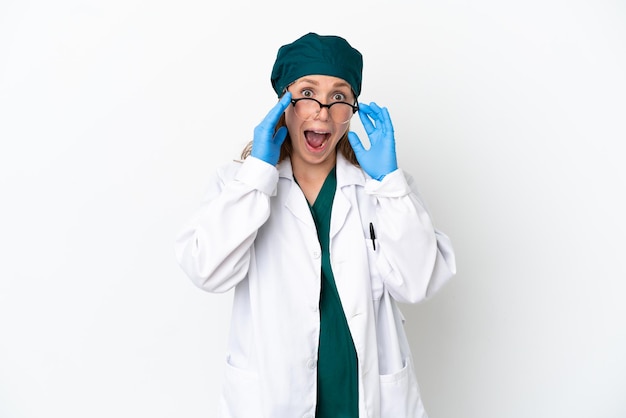 Cirujano mujer caucásica en uniforme verde aislado sobre fondo blanco con gafas y sorprendido