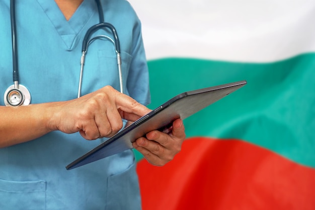 Cirujano o médico con una tableta digital en el fondo de la bandera de Bulgaria