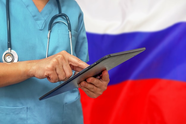 Cirujano o médico con una tableta digital en el fondo de la bandera de Rusia