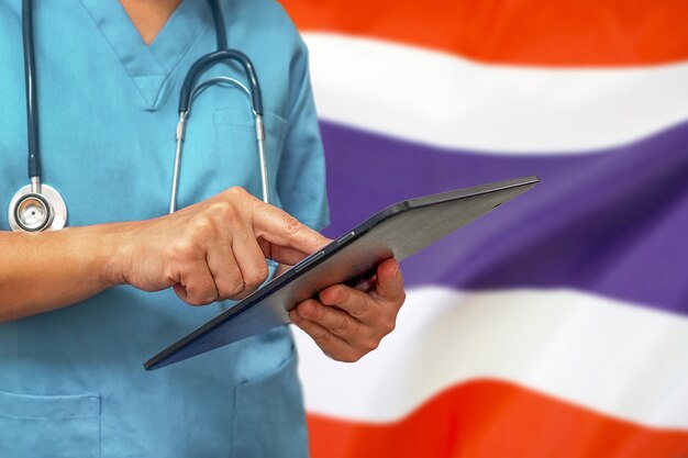 Cirujano o médico con una tableta digital en el fondo de la bandera de Tailandia