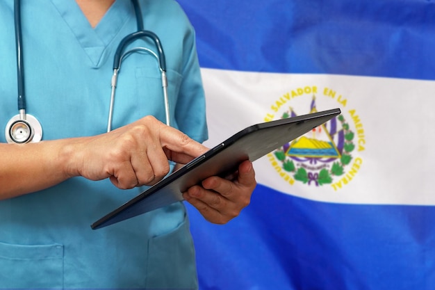 Cirujano o médico usando una tableta digital en el fondo de la bandera de El Salvador