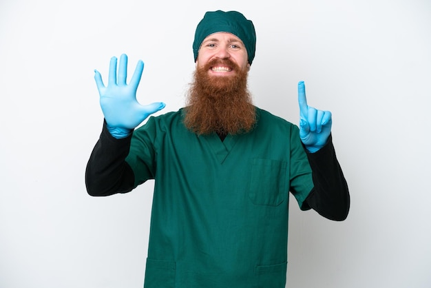 Cirujano pelirrojo con uniforme verde aislado de fondo blanco contando seis con los dedos