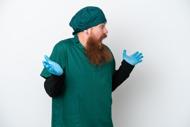 Cirujano pelirrojo con uniforme verde aislado de fondo blanco con expresión facial sorpresa