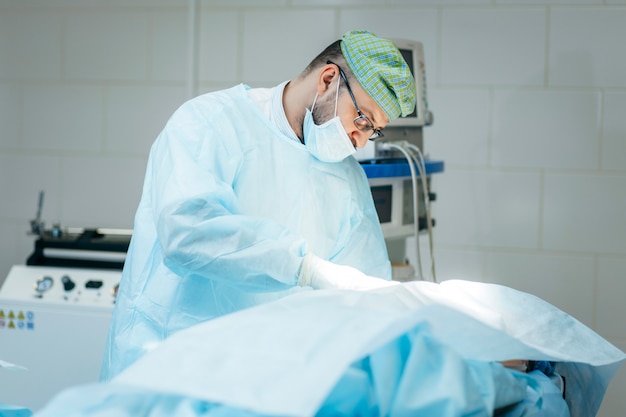 Cirujano realizando cirugía de senos en quirófano de hospital. Cirujano en máscara con lupas quirúrgicas durante el procedimiento médico.