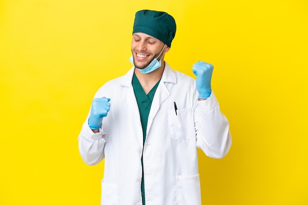 Cirujano rubio con uniforme verde aislado de fondo amarillo celebrando una victoria