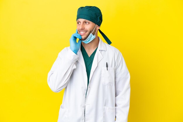 Cirujano rubio con uniforme verde aislado de fondo amarillo pensando en una idea mientras mira hacia arriba