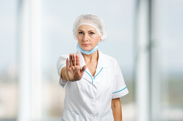 Cirujano de sexo femenino maduro que gesticula la parada. Seguro médico mujer mostrar gesto de parada.