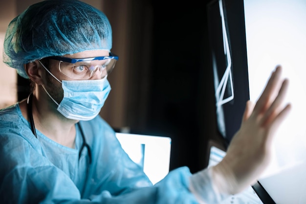 cirujano con uniforme y gafas examina una imagen de rayos X de una fractura ósea en el quirófano