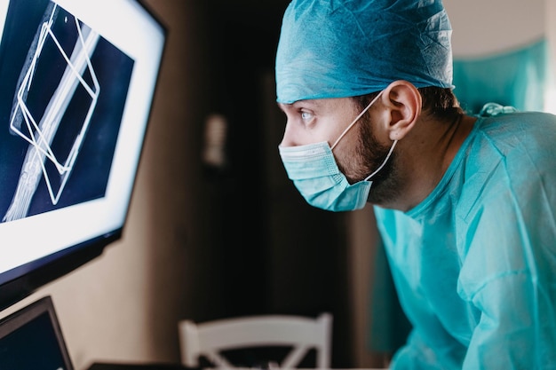 cirujano con uniforme y gafas examina una imagen de rayos X de una fractura ósea en el quirófano