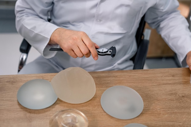 Cirujano con uniforme de medicina sosteniendo nuevos implantes en las manos. Doctor en máscara que muestra implantes médicos de silicona.