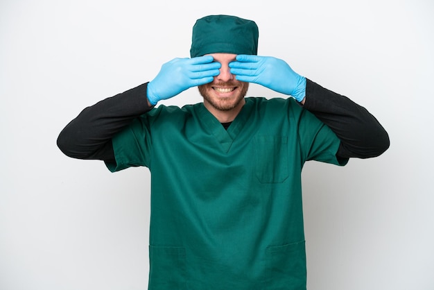 Cirurgião brasileiro de uniforme verde isolado no fundo branco, cobrindo os olhos pelas mãos