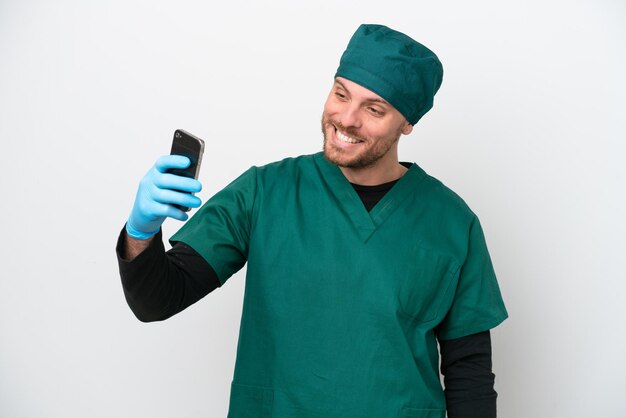 Cirurgião brasileiro de uniforme verde isolado no fundo branco fazendo uma selfie