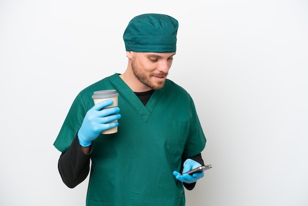 Cirurgião brasileiro de uniforme verde isolado no fundo branco segurando café para levar e um celular
