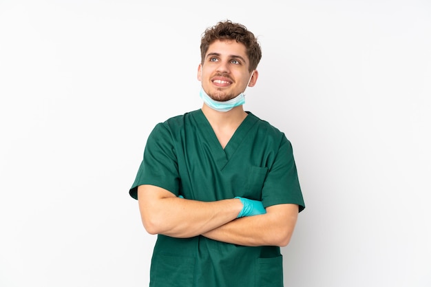 Cirurgião de uniforme verde isolado em branco isolado olhando para cima enquanto sorri