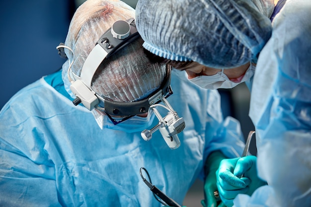 Cirurgião e seu assistente realizando cirurgia plástica na sala de cirurgia do hospital. cirurgião na máscara usando lupas durante procedimento médico.