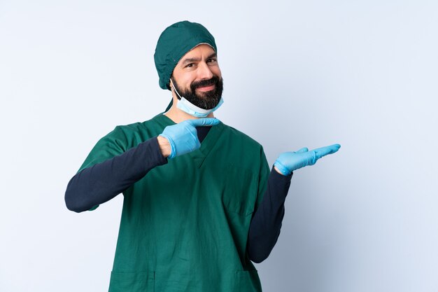 Cirurgião homem de uniforme verde sobre parede isolada, segurando copyspace imaginário na palma da mão para inserir um anúncio