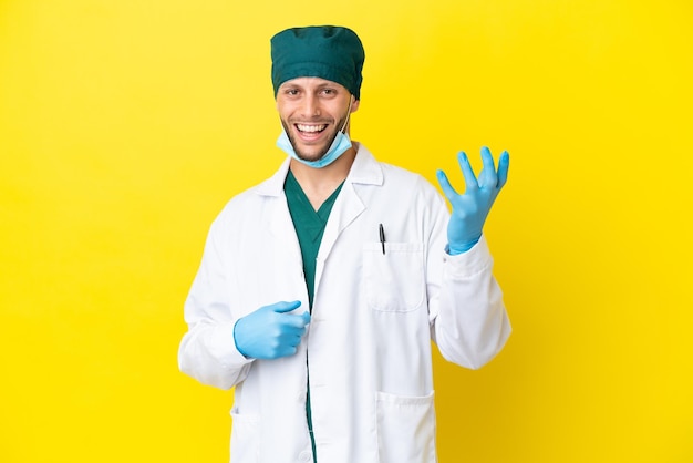 Cirurgião loiro de uniforme verde isolado em fundo amarelo fazendo gesto de guitarra