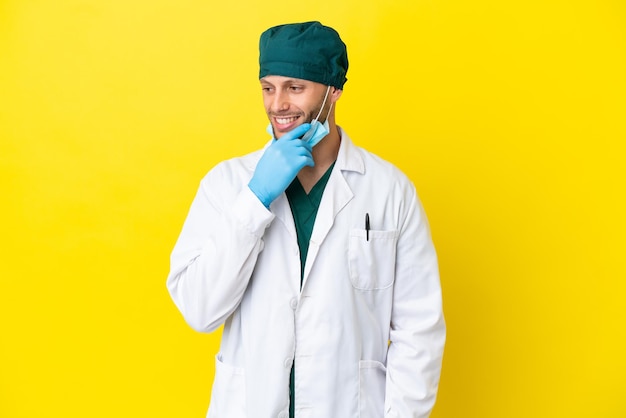 Cirurgião loiro de uniforme verde isolado em fundo amarelo, olhando para o lado