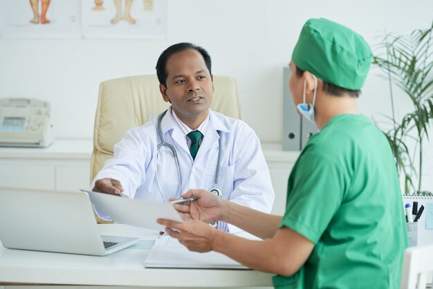 Cirurgião mostrando os resultados dos exames médicos do paciente ao clínico geral e discutindo a forma de tratamento