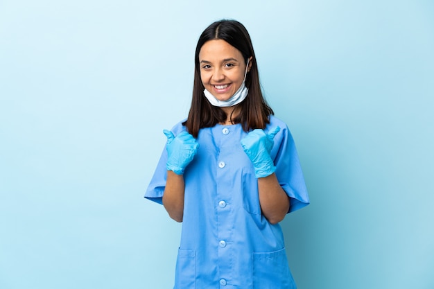 Foto cirurgião mulher sobre parede azul com polegares para cima gesto e sorrindo