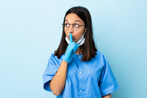 Cirurgião mulher sobre parede azul, mostrando um sinal de silêncio gesto colocando o dedo na boca