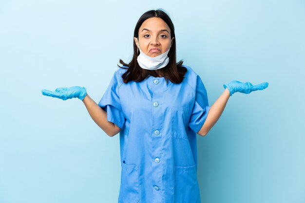 Cirurgião mulher sobre parede azul, tendo dúvidas ao levantar as mãos