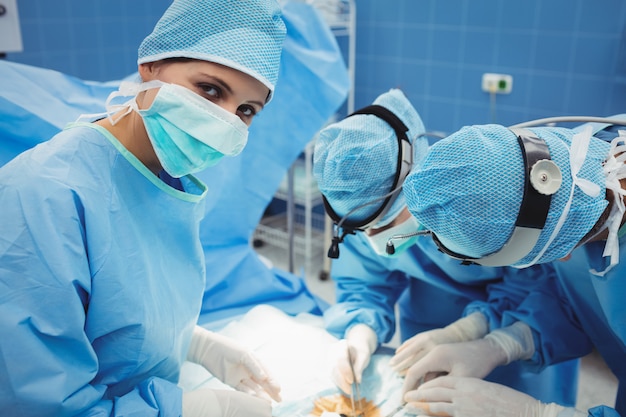 Cirurgião, olhando para a câmera enquanto colegas realizando operação