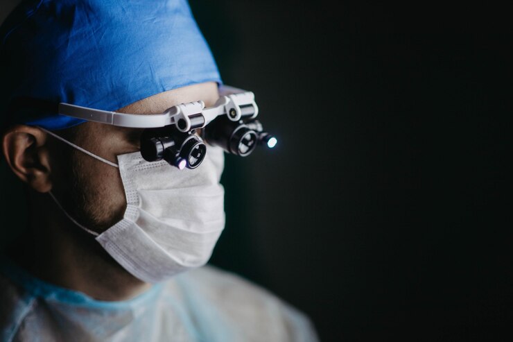 Foto cirurgião usando lupas binoculares opera em um paciente em uma sala de cirurgia escura