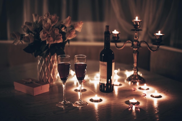 Cita a la luz de las velas Copas con velas de vino ramo de rosas y caja de regalo en la mesa Cena romántica a la luz de las velas en casa por la noche