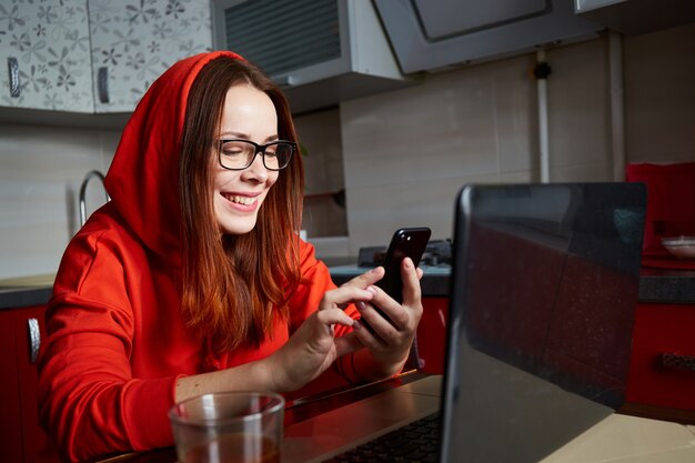 Citas en línea. Retrato de mujer pelirroja complacida sentada en la cocina y hacer videollamadas en la computadora portátil