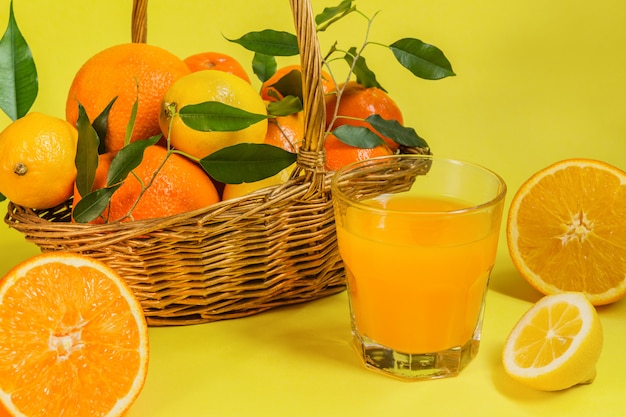 Los cítricos de limón naranja en una canasta y un jugo sobre un fondo amarillo alimentan una dieta saludable