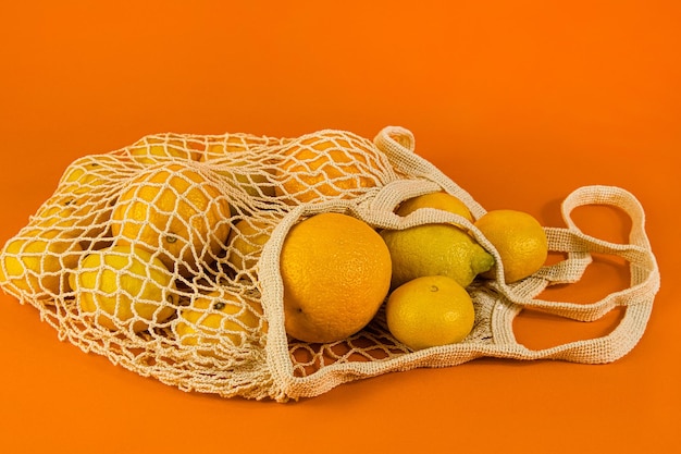 Los cítricos naranja, limón, mandarina se encuentran en una bolsa de algodón, una bolsa de hilo sobre un fondo naranja.